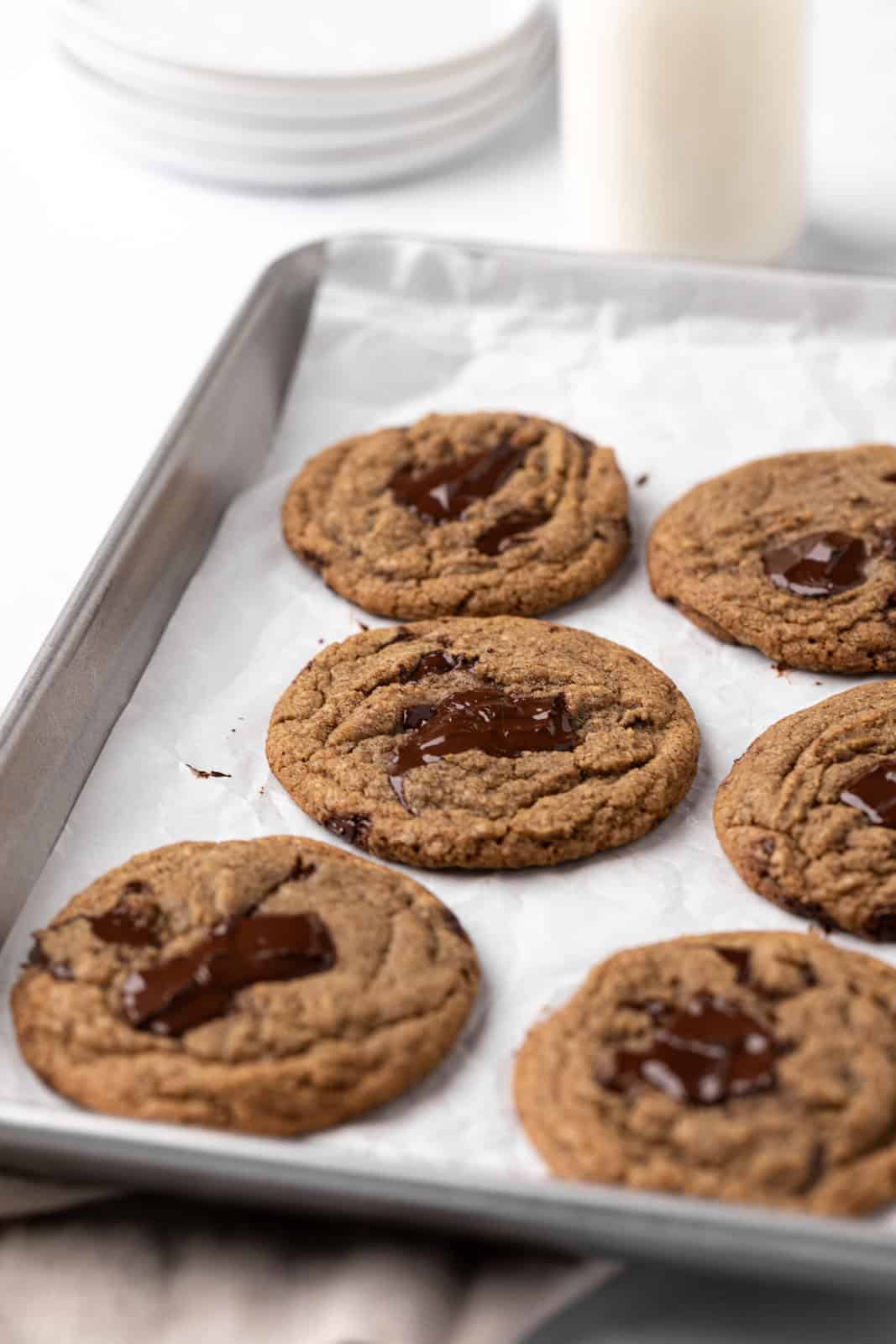 Six baked coffee chocolate chip cookies set on a parchment-lined sheet pan.