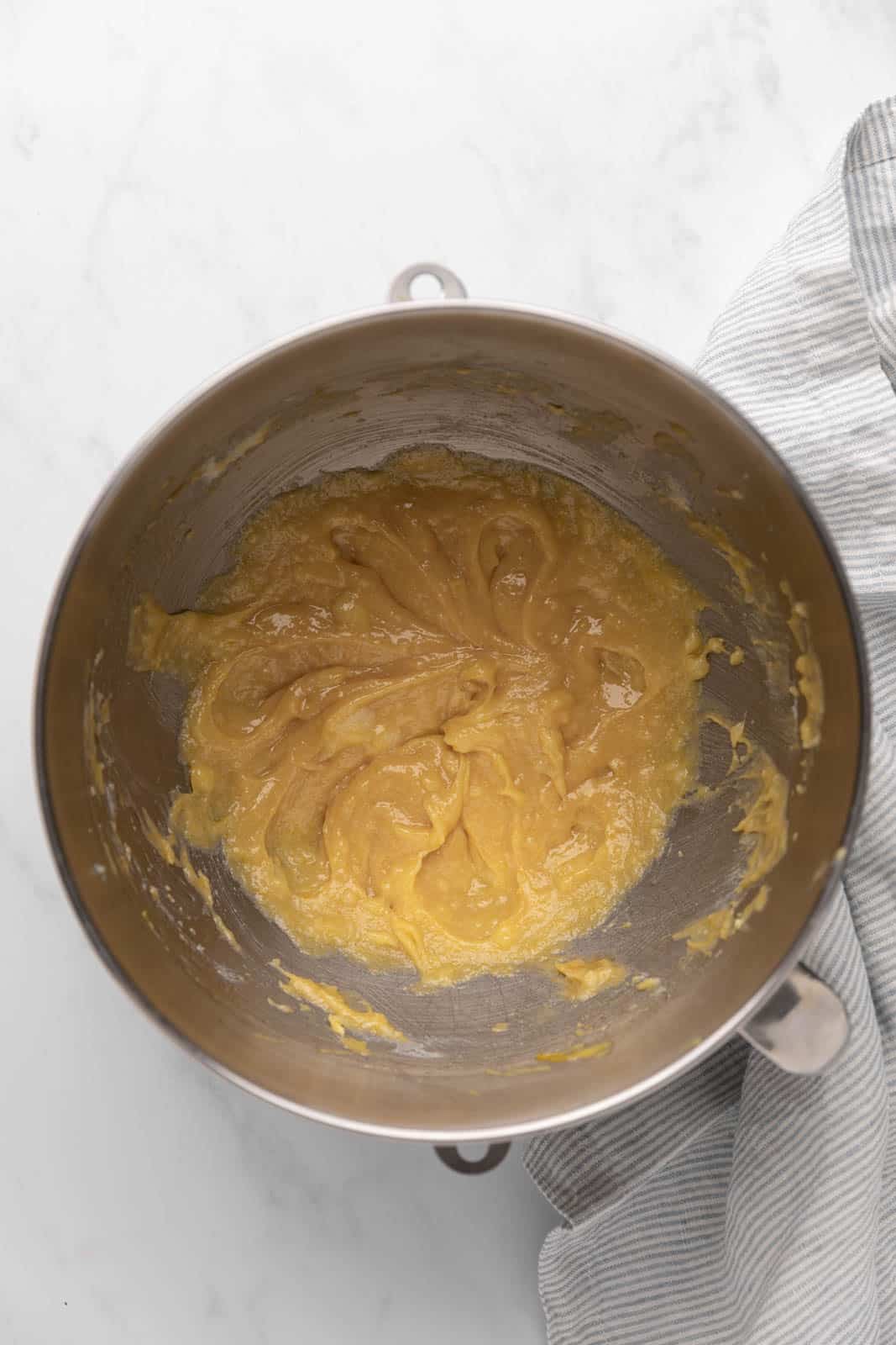 Egg and vanilla extract mixed into cream butter and sugar mixture in a metal mixing bowl set on a flat surface.