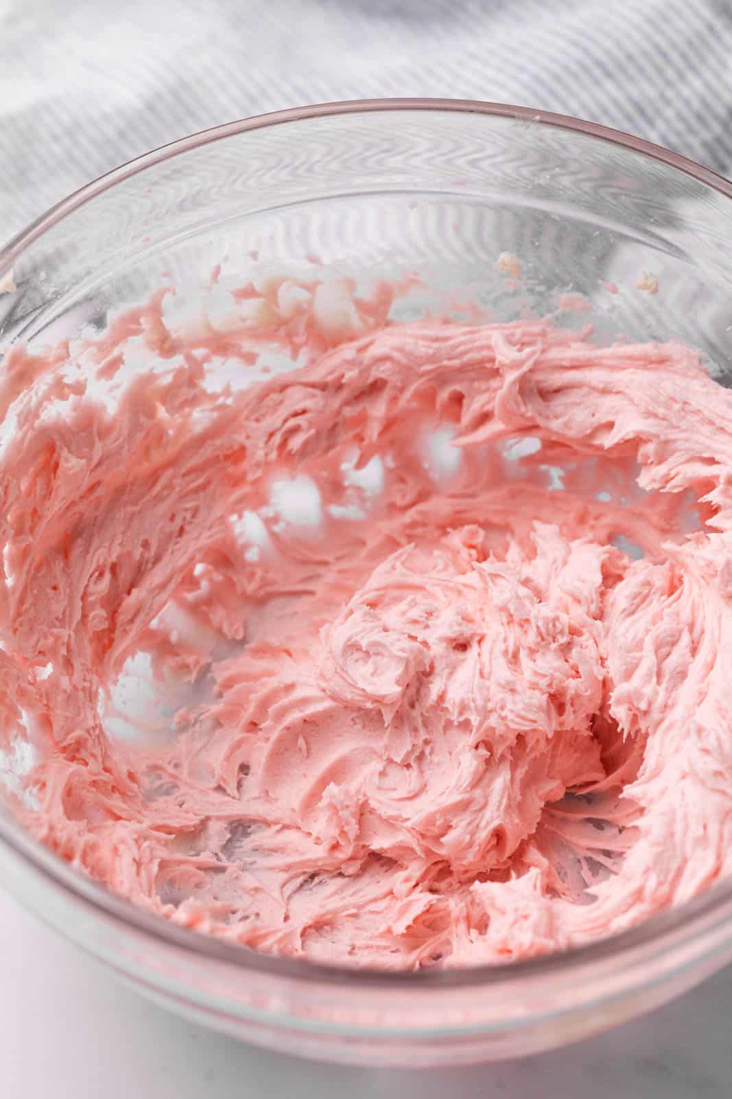 Close up of pink buttercream frosting mixed in a glass mixing bowl.