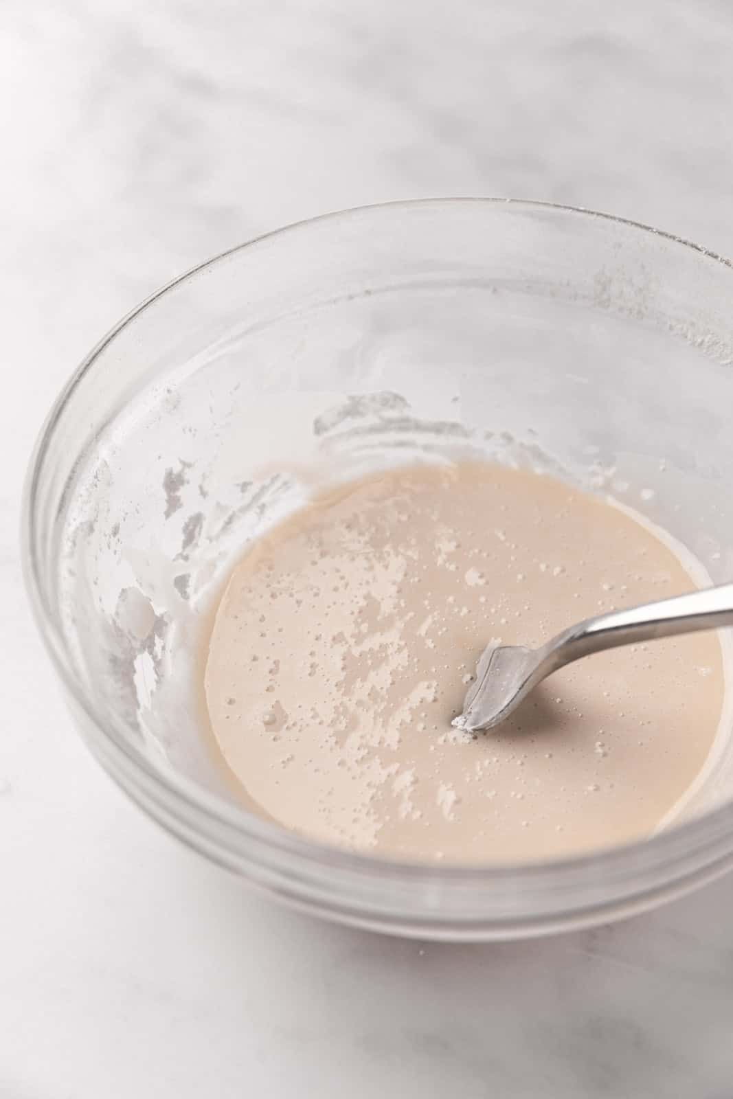 Mixed vanilla glaze in a glass mixing bowl with a fork set on a flat surface.