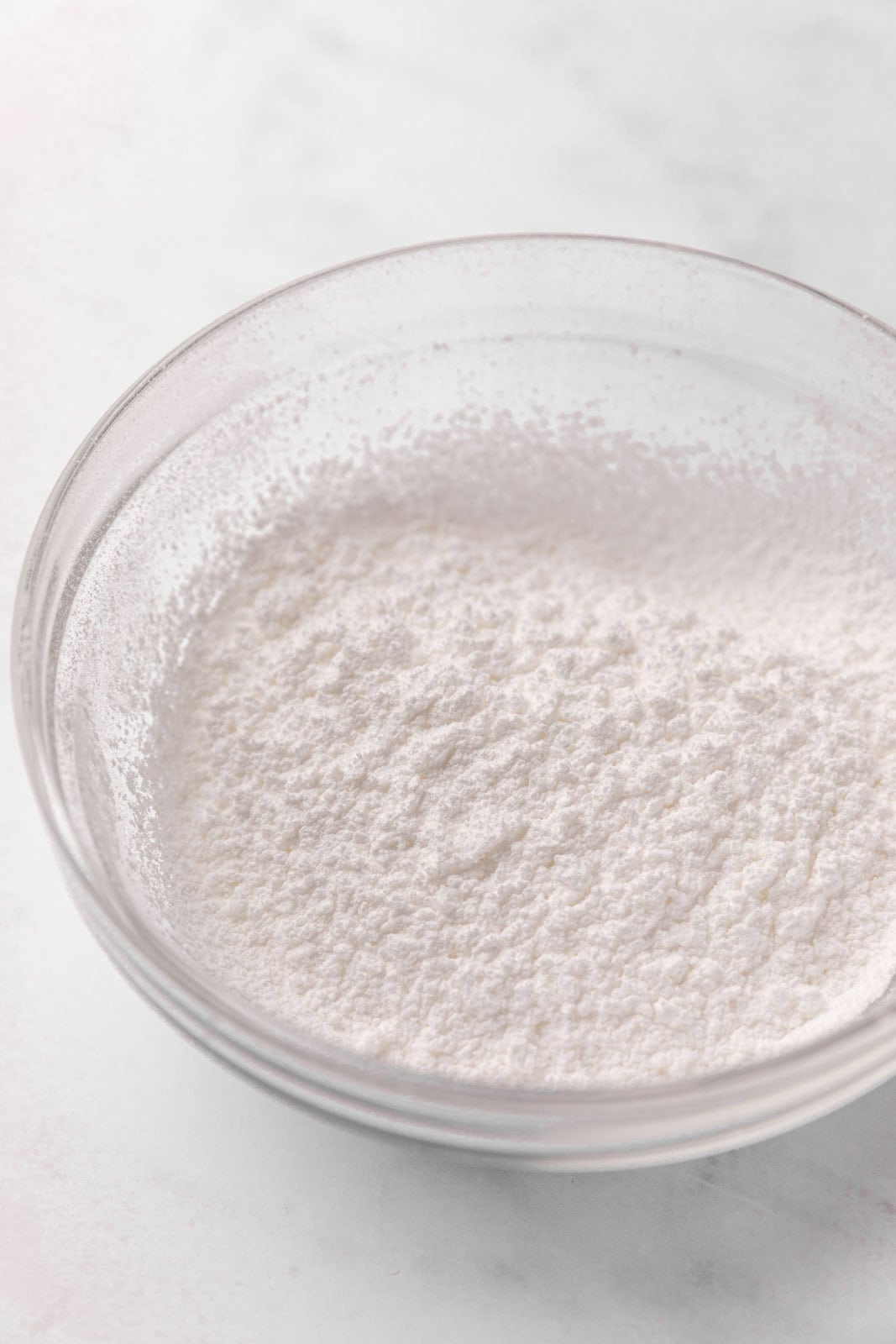 Sifted powdered sugar in a glass mixing bowl set on a flat surface.