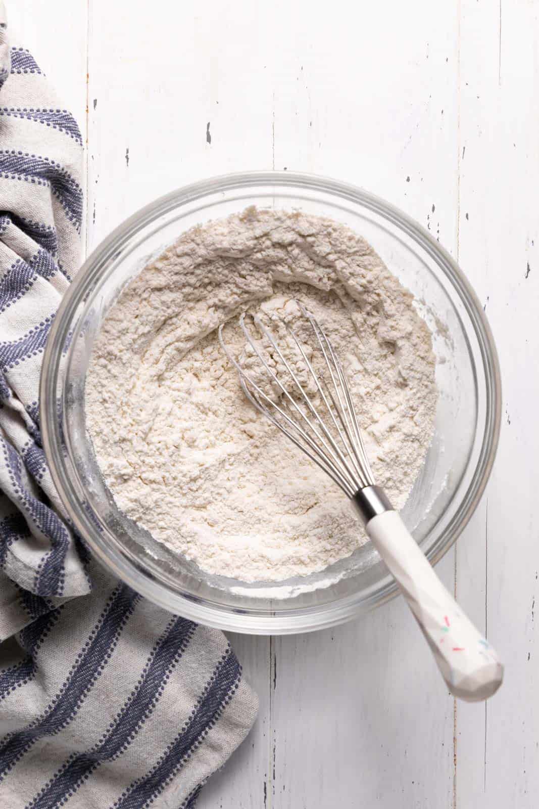 Whisked dry ingredients with a whisk in a glass mixing bowl set on a flat surface.