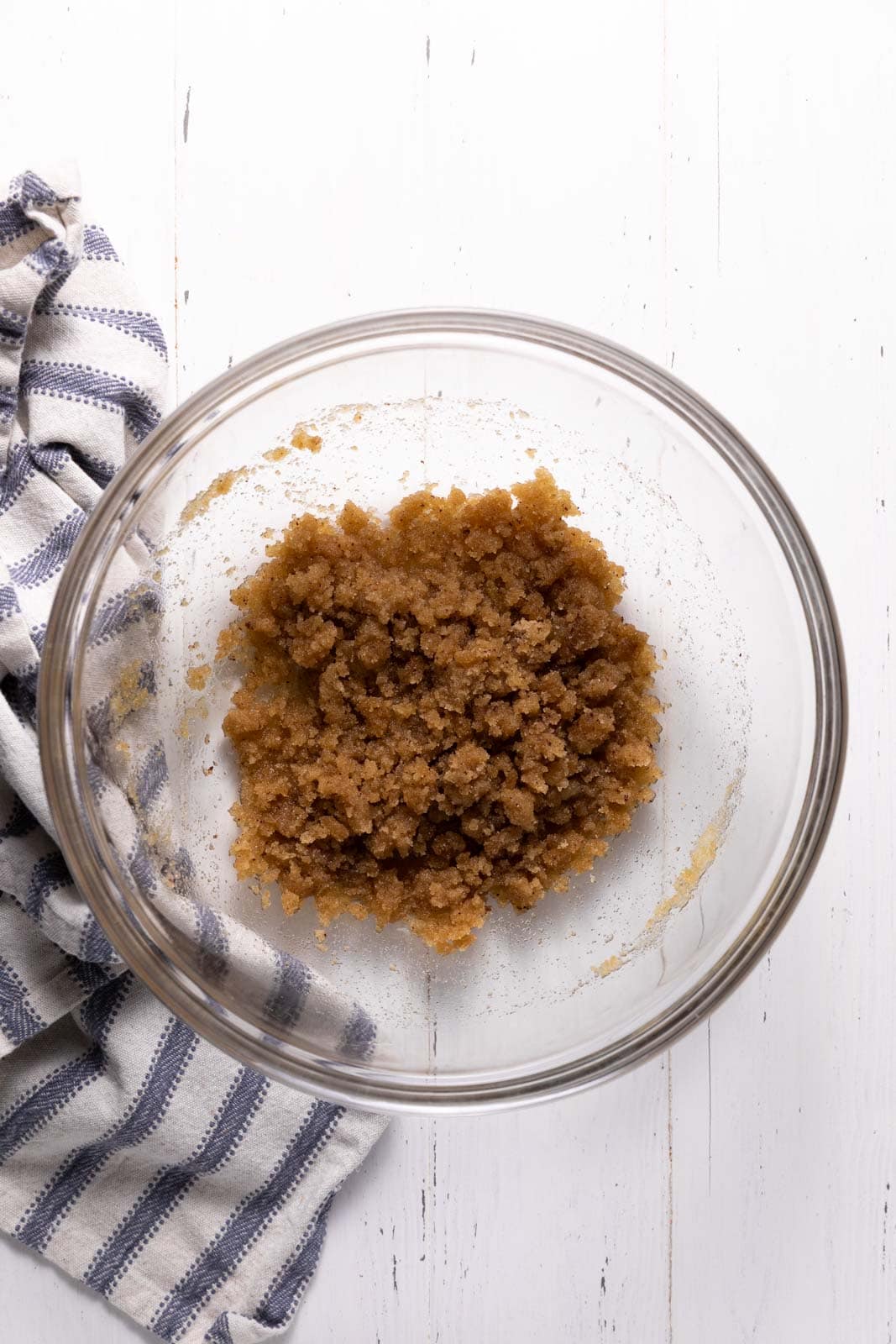Whisked brown butter and sugar in a glass mixing bowl set on a flat surface.