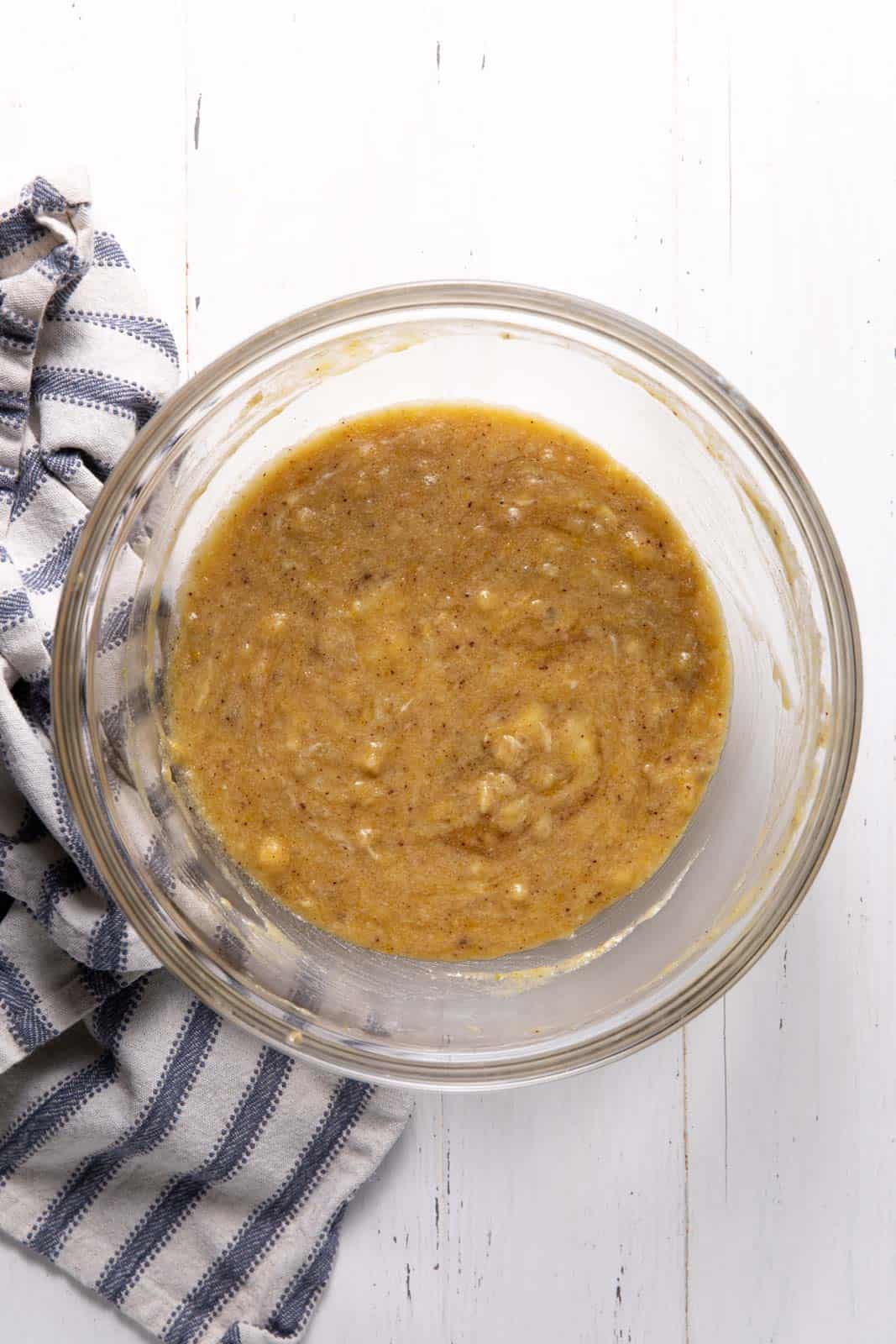 Wet ingredients whisked with brown butter and sugar in a glass mixing bowl set on a flat surface.