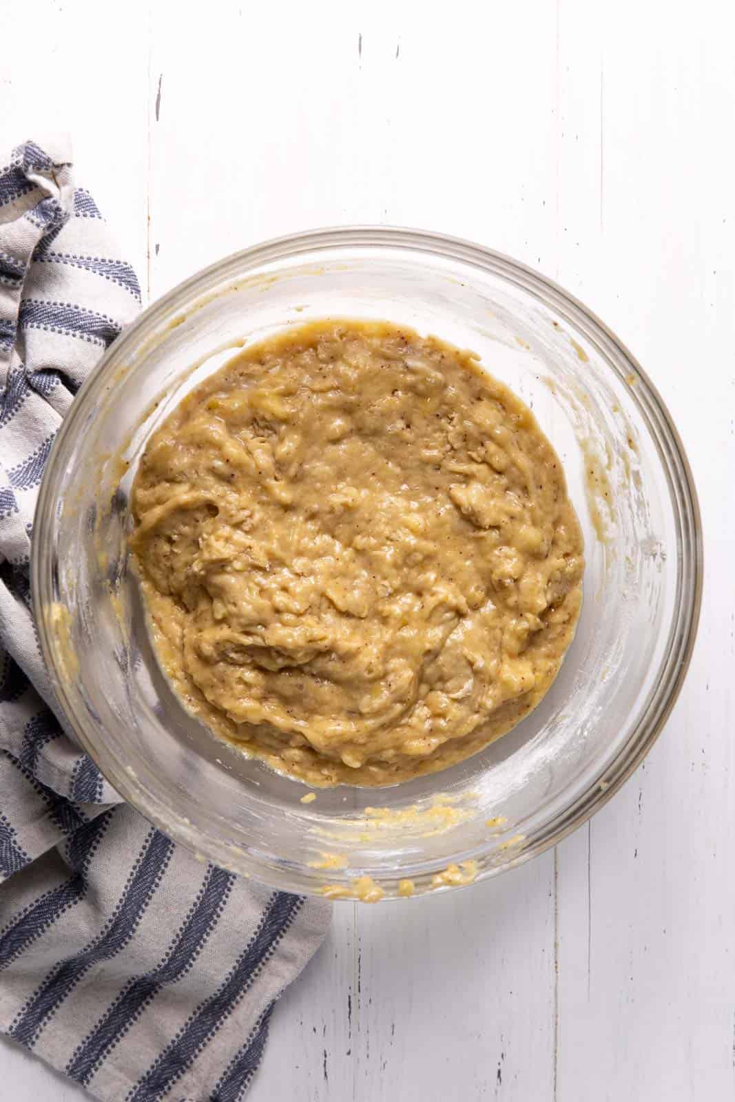 Banana bread batter in a glass mixing bowl set on a flat surface.