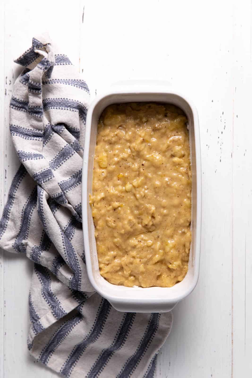 Banana bread batter in a ceramic loaf pan set on a flat surface.