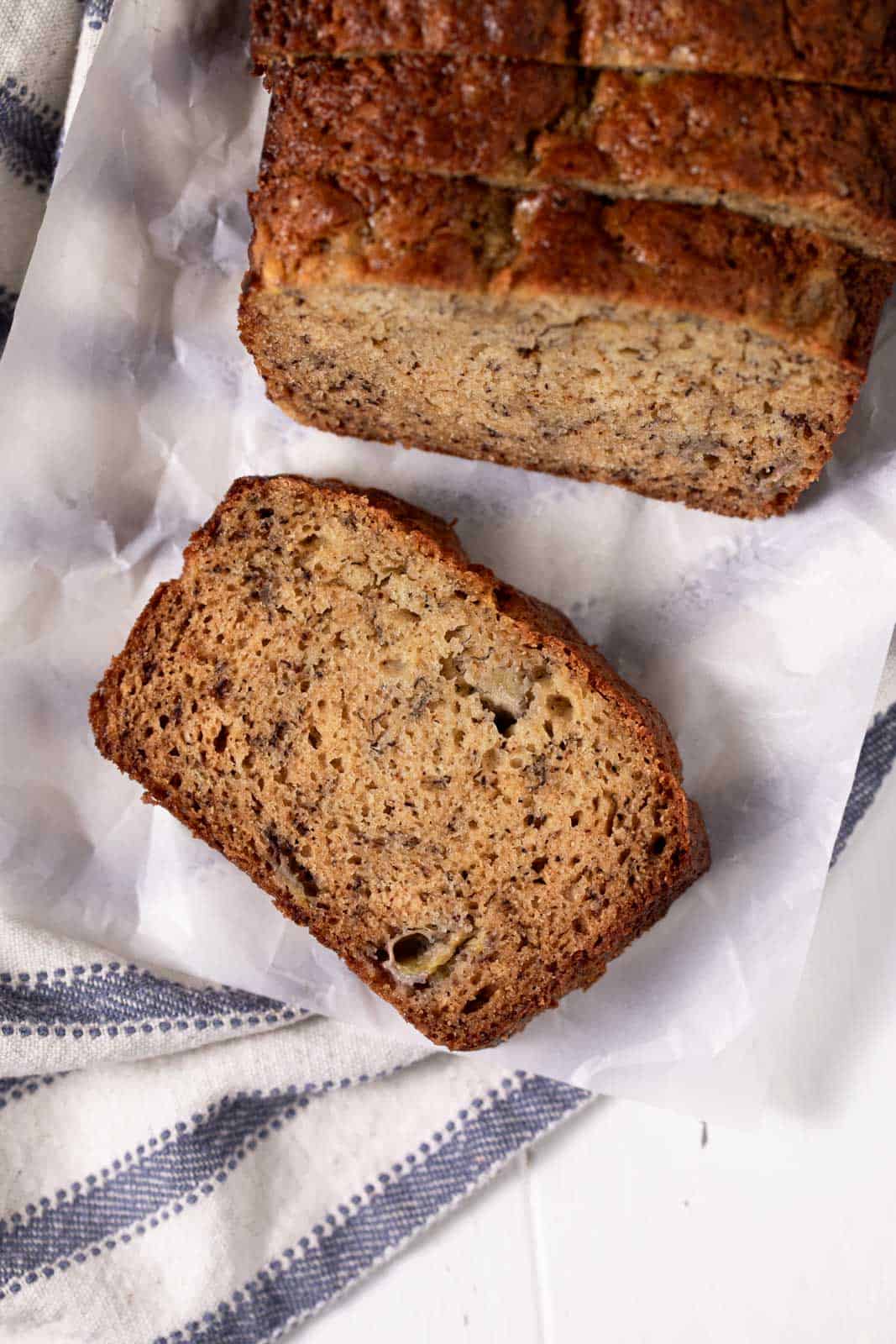 Overhead shot of a slice of banana bread with 2 bananas on a piece of parchment paper.