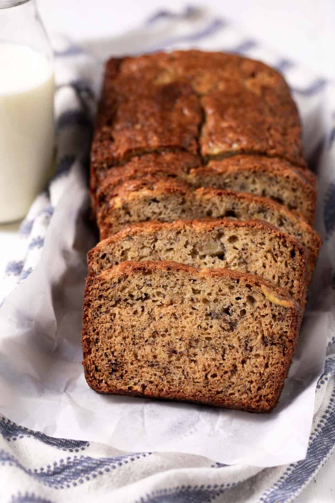 Loaf of banana bread with 2 bananas half sliced on a parchment paper over a linen napkin.