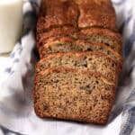 Loaf of banana bread with 2 bananas half sliced on a parchment paper over a linen napkin.