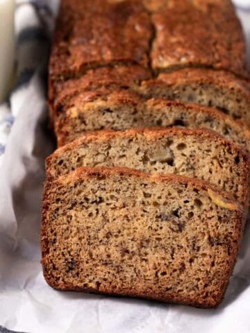 Loaf of banana bread with 2 bananas half sliced on a parchment paper over a linen napkin.