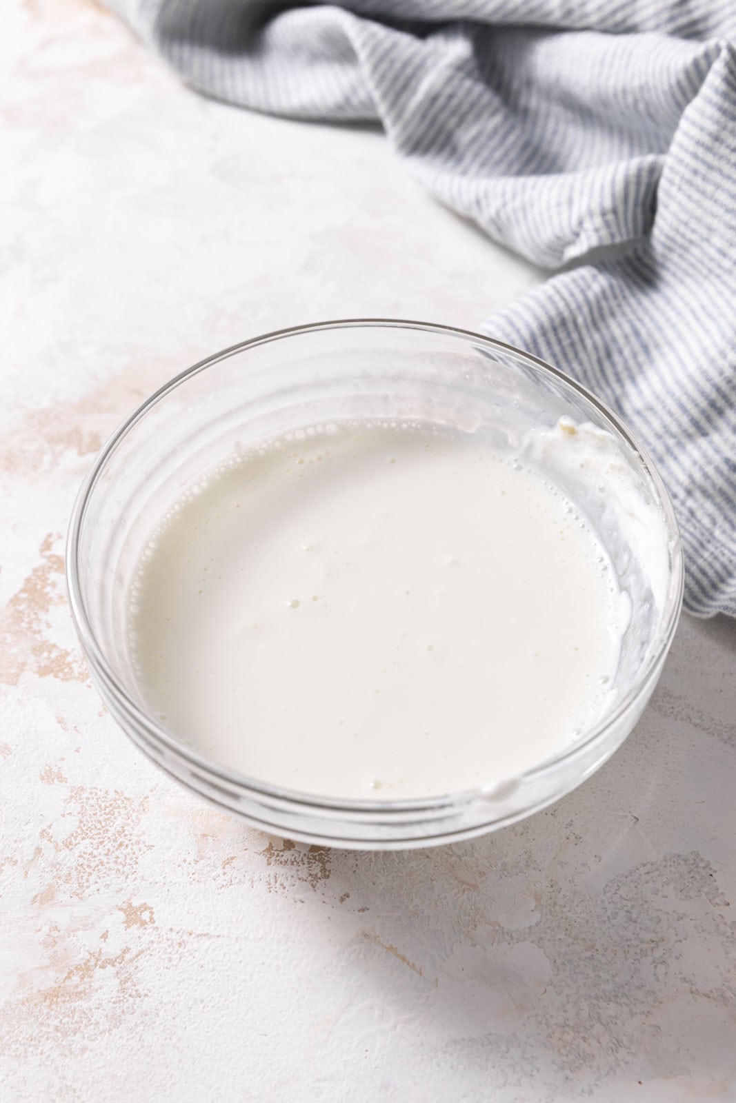 Whisked sour cream and milk in a small glass mixing bowl set on a flat surface.