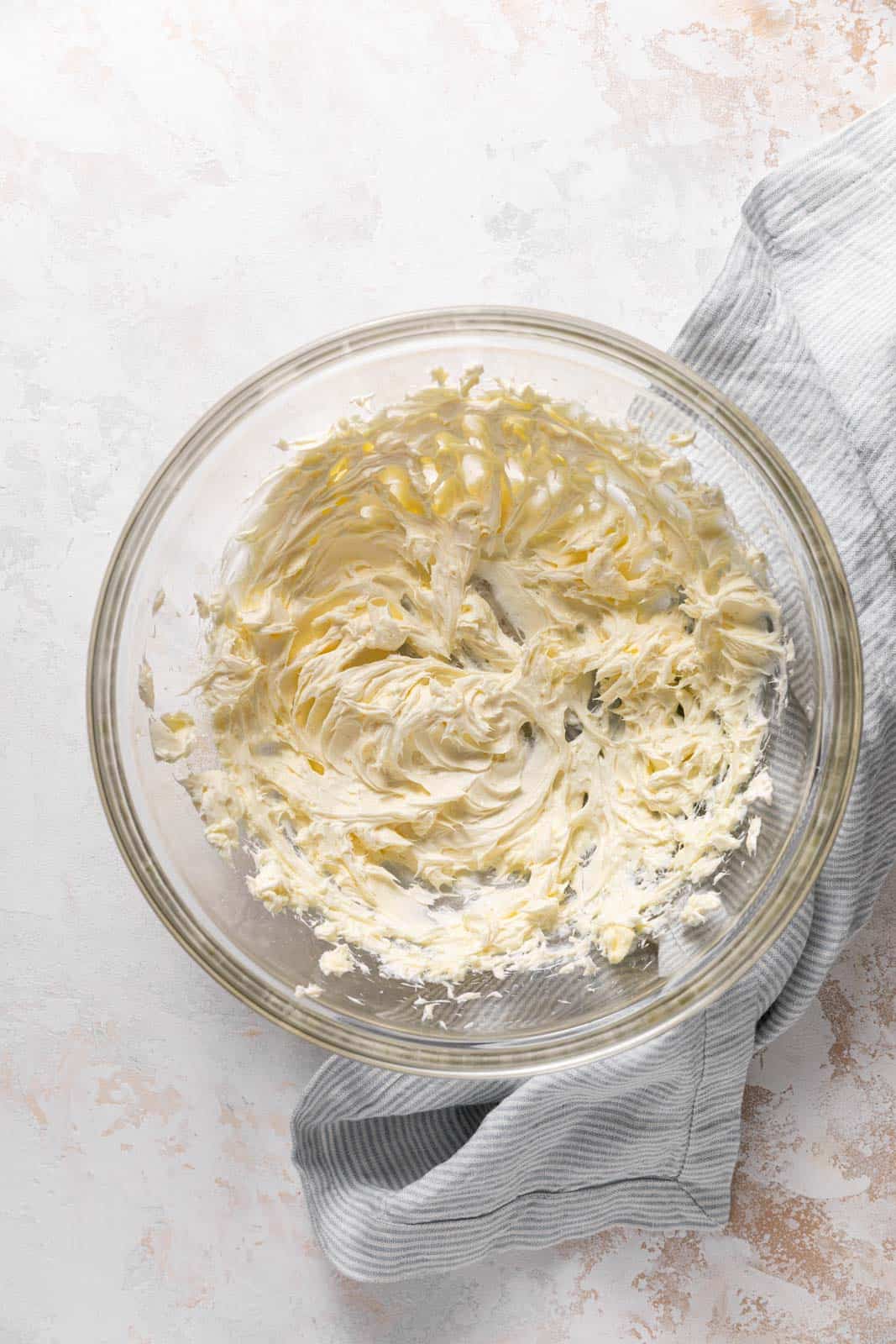 Creamed butter and cream cheese in a glass mixing bowl set on a flat surface.