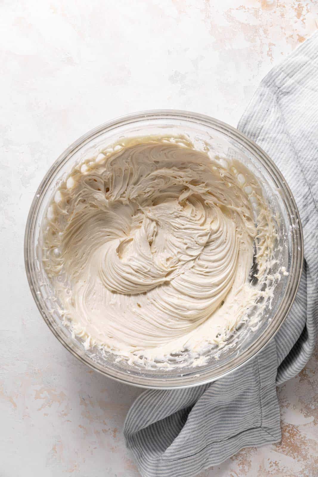 Close up of brown sugar cream cheese frosting in a glass mixing bowl set on a flat surface.