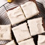 Brown sugar cream cheese frosting spread over banana cake cut into squares on a round wire rack.