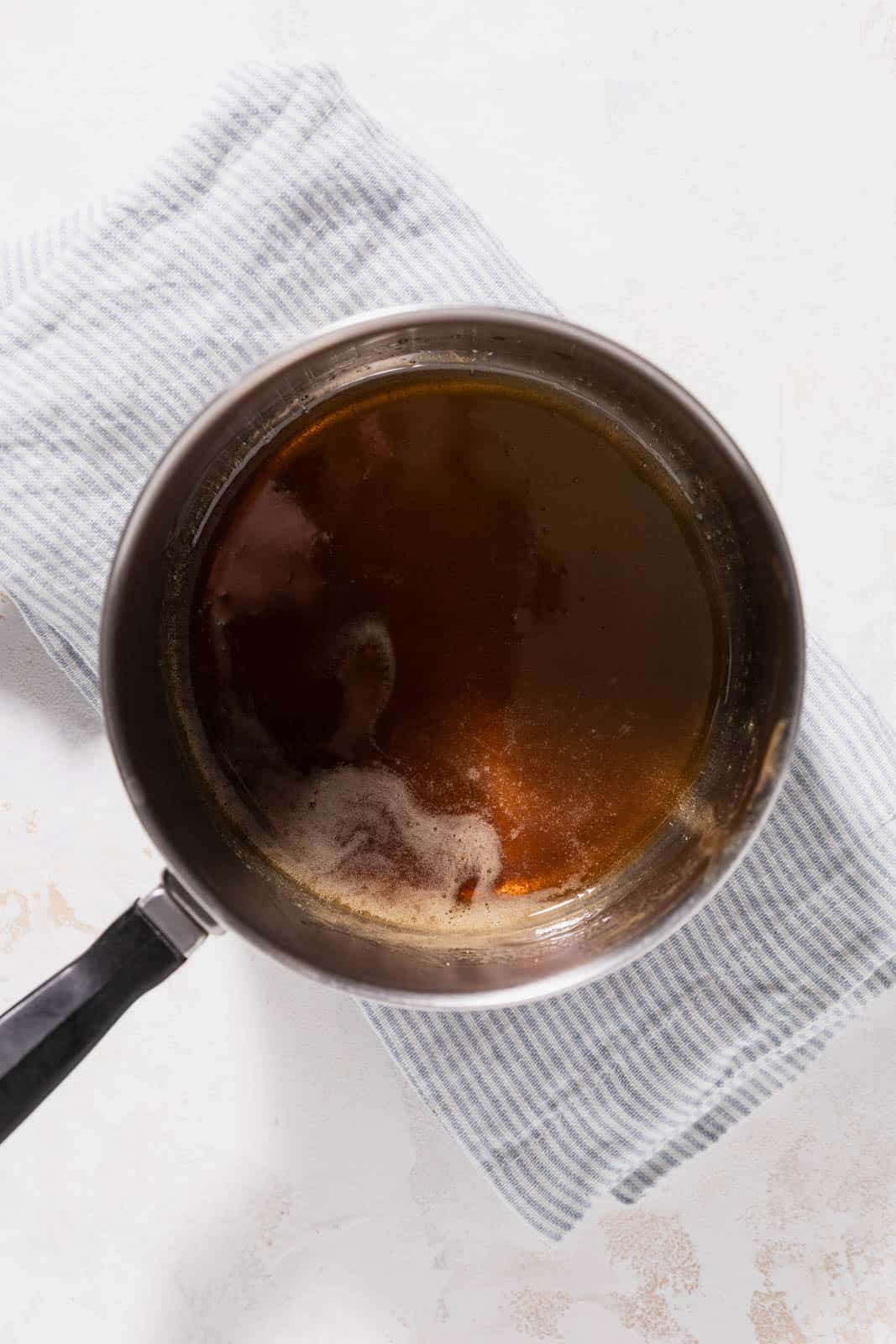 Melted brown sugar with water in a small saucepan set over a linen on a flat surface.