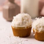 Close up of coconut cupcake with coconut sprinkled on the frosting set on a wood board.