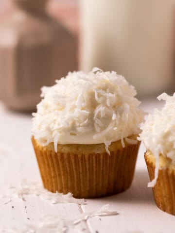 Close up of coconut cupcake with coconut sprinkled on the frosting set on a wood board.