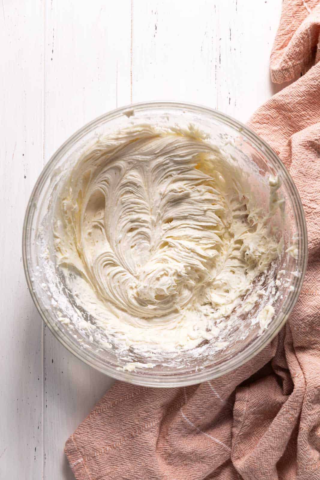 Coconut cream cheese frosting mixed in a glass mixing bowl set on a flat.