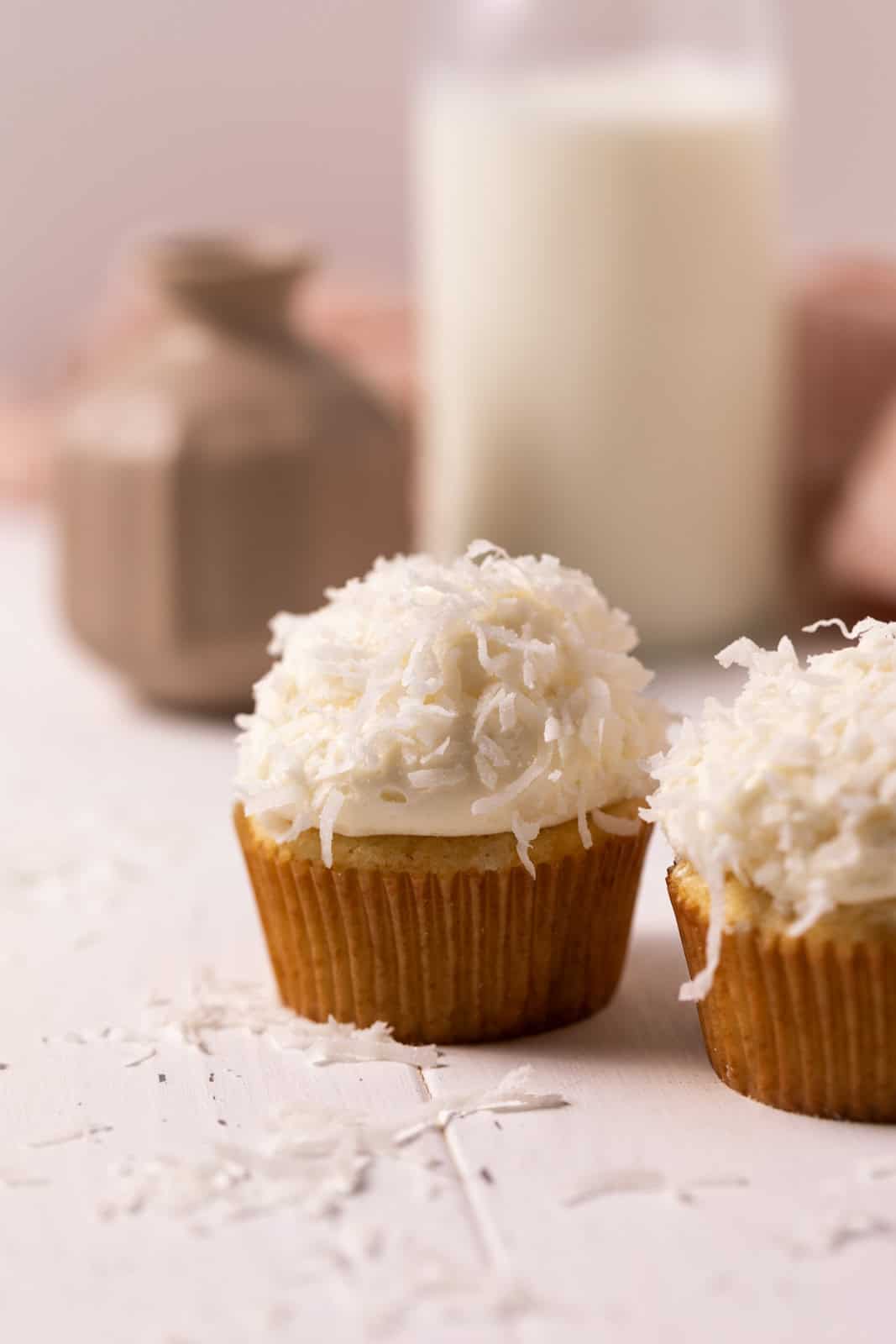 Close up of coconut cupcake with coconut sprinkled on the frosting set on a wood board.