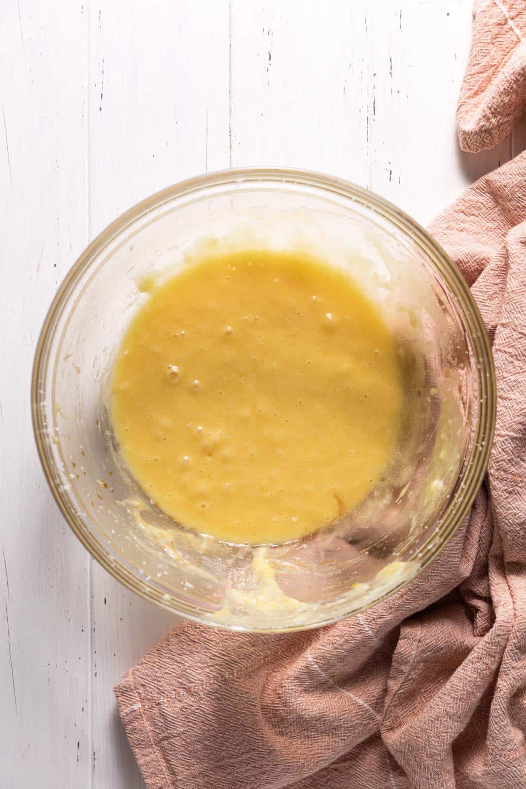 Eggs mixed into creamed butter and sugar in a glass mixing bowl set on a flat surface.