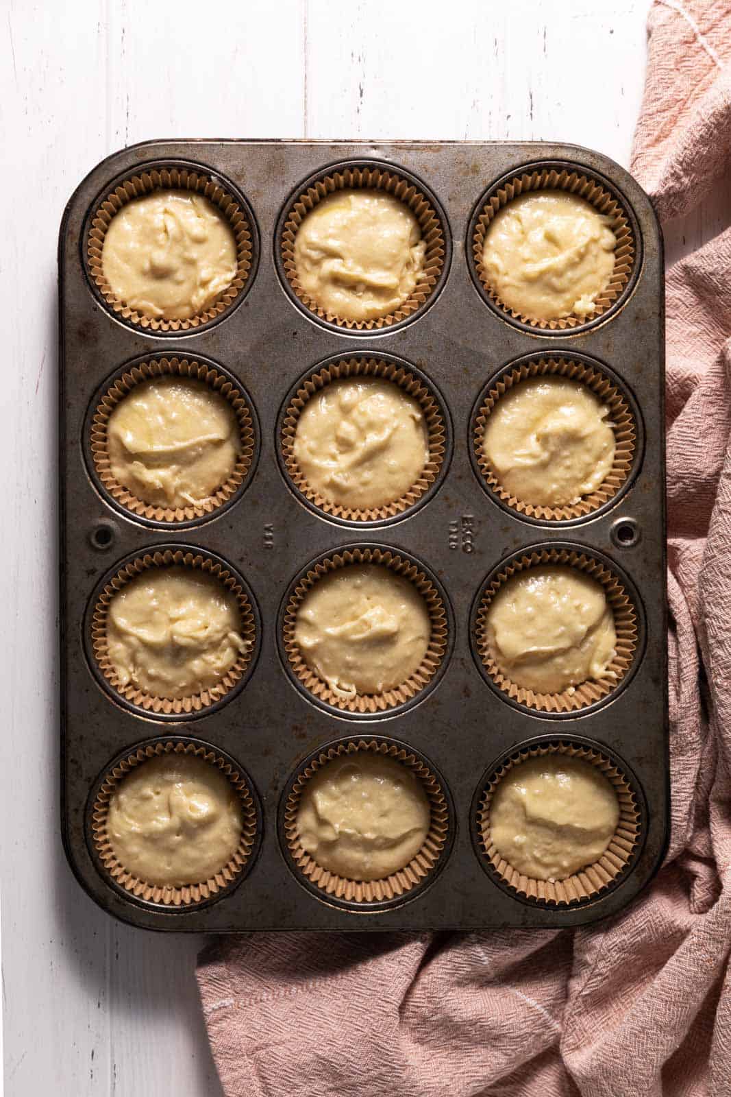 Coconut cupcake batter in a 12 count muffin tin with cupcake liners.