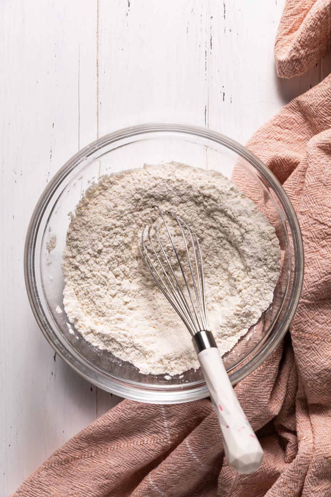 Whisked dry ingredients in a glassmixing set on a flat surface with a whisk.