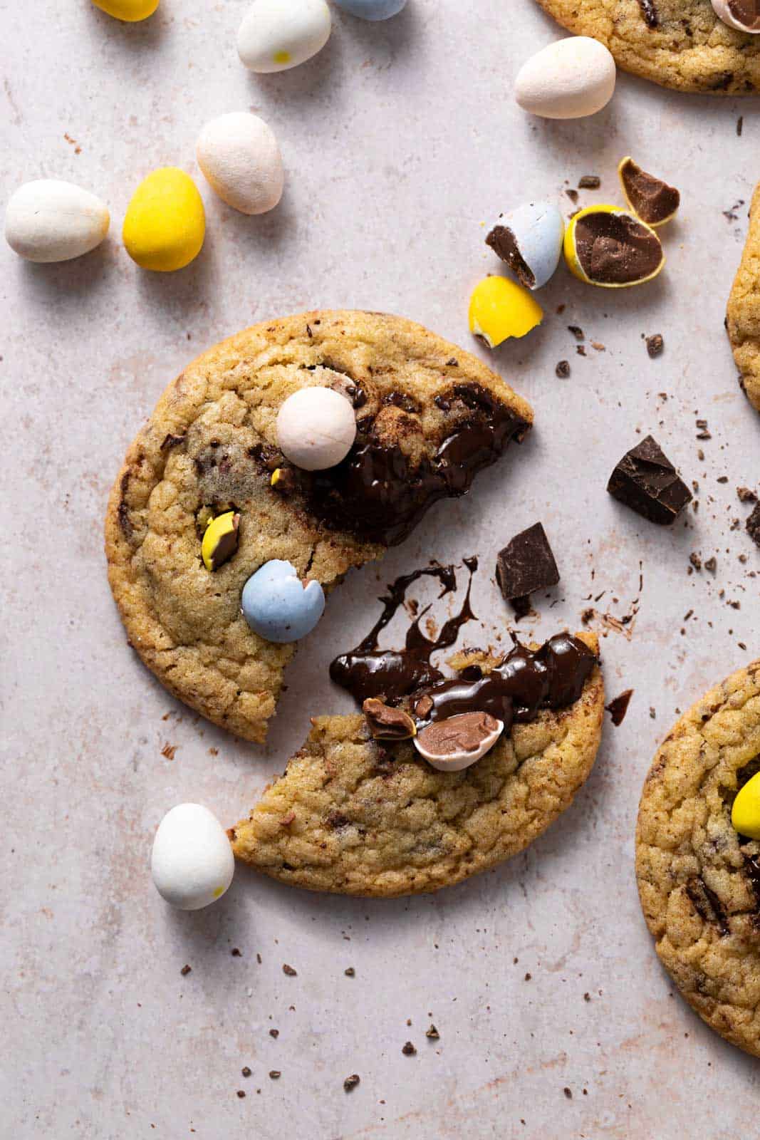 Close up of one mini egg cookie broken in half with chocolate egg candies around set on a flat surface.