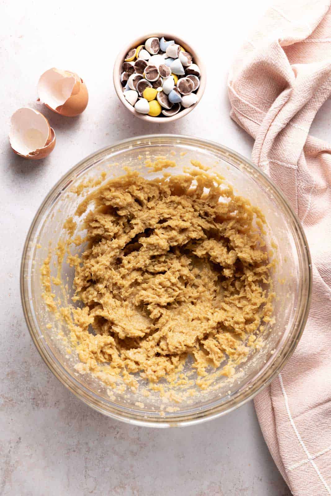 Creamed butter and sugar mixed with eggs and vanilla in a glass mixing bowl set on a flat surface.