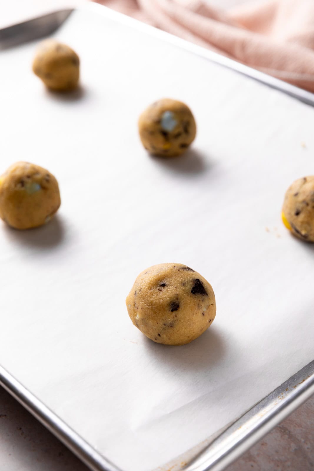 Mini egg cookie dough rolled into balls and set on spread out on a parchment lined sheet pan.