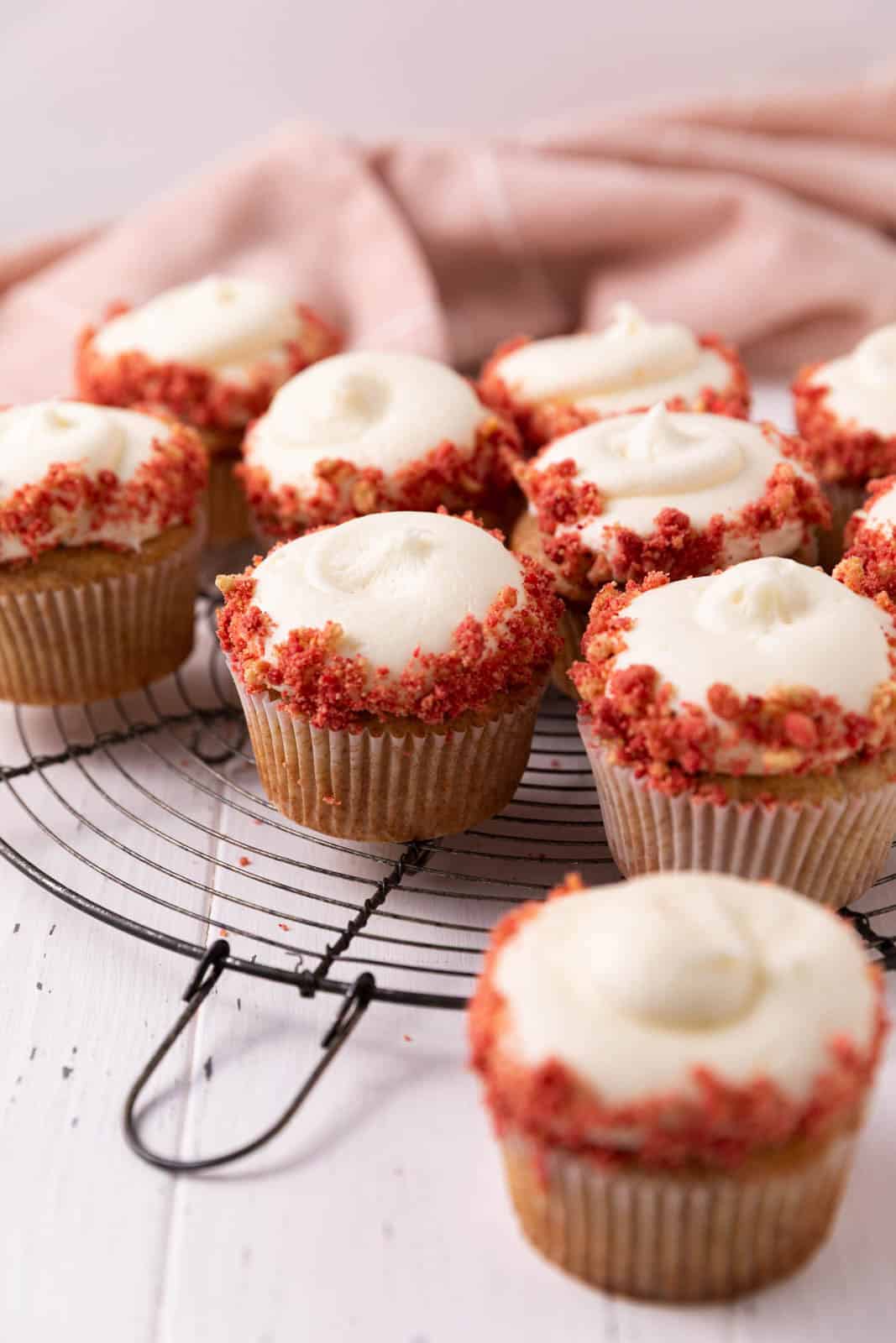 Strawberry crunch cupcakes with cream cheese frosting on a round wire rack.