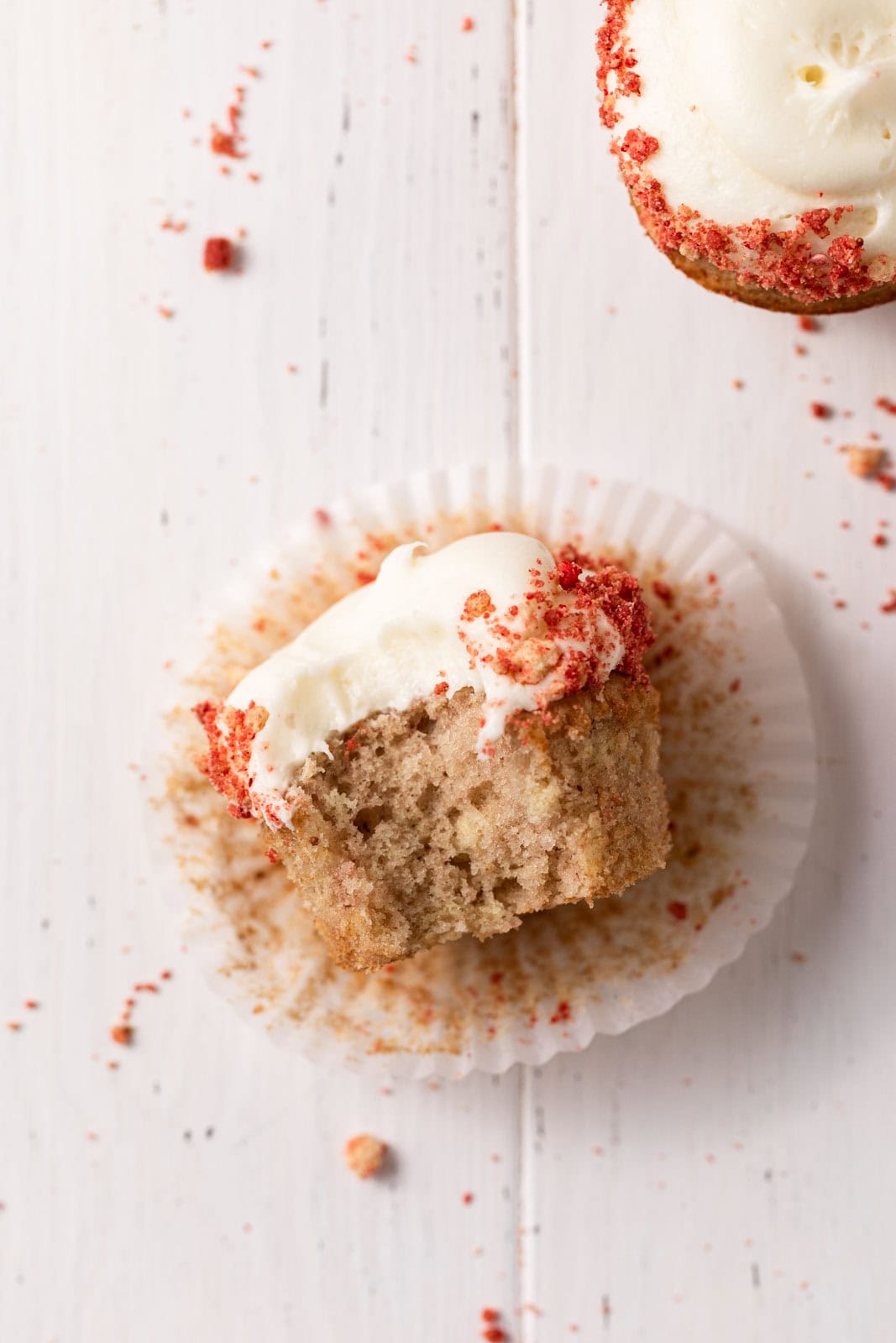 Overhead shot of a strawberry crunch cupcake with cream cheese frosting on its side with a bite taken out of it.