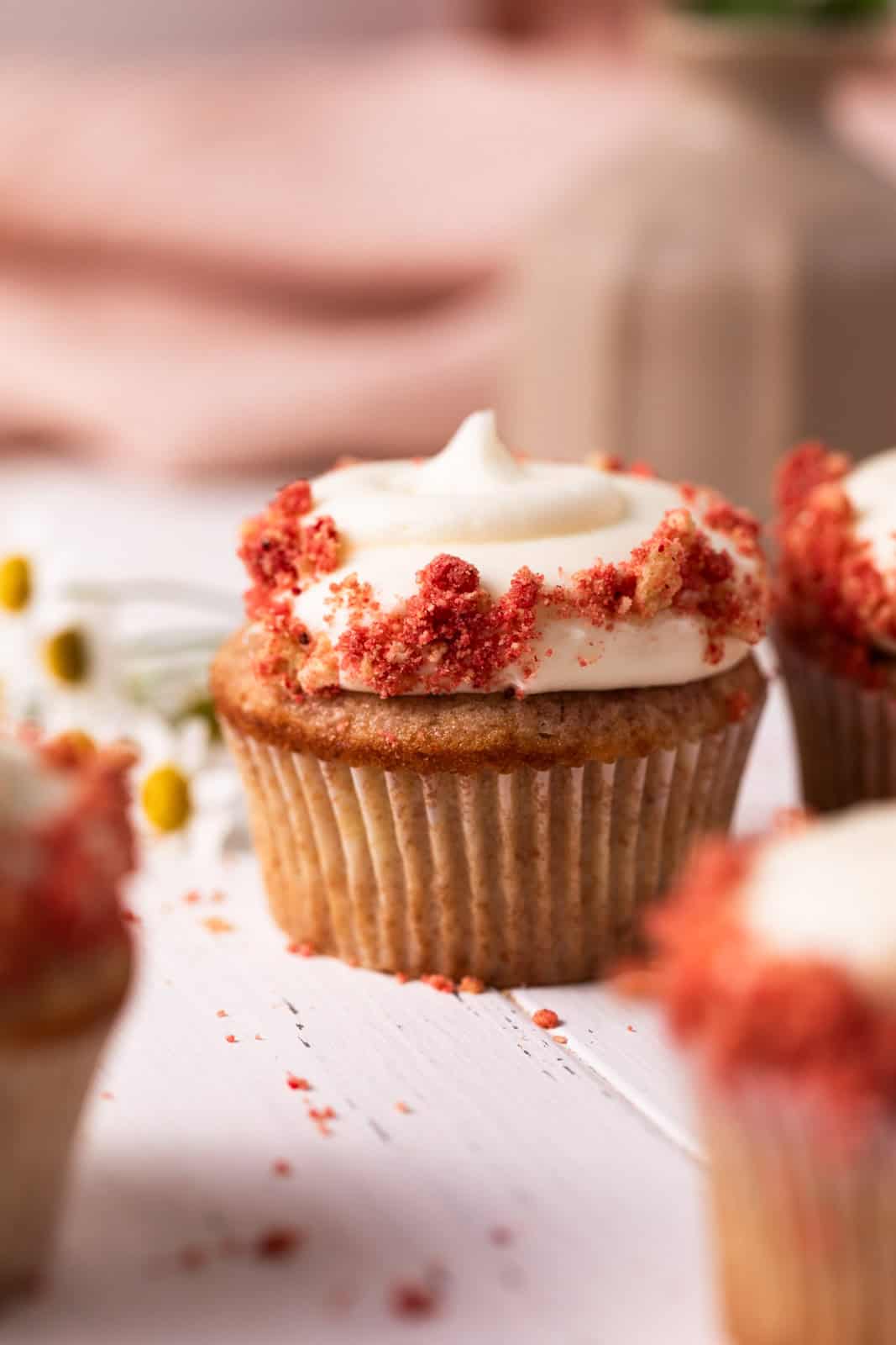 Close up of strawberry crunch cupcake with cream cheese frosting set on a white wood board.