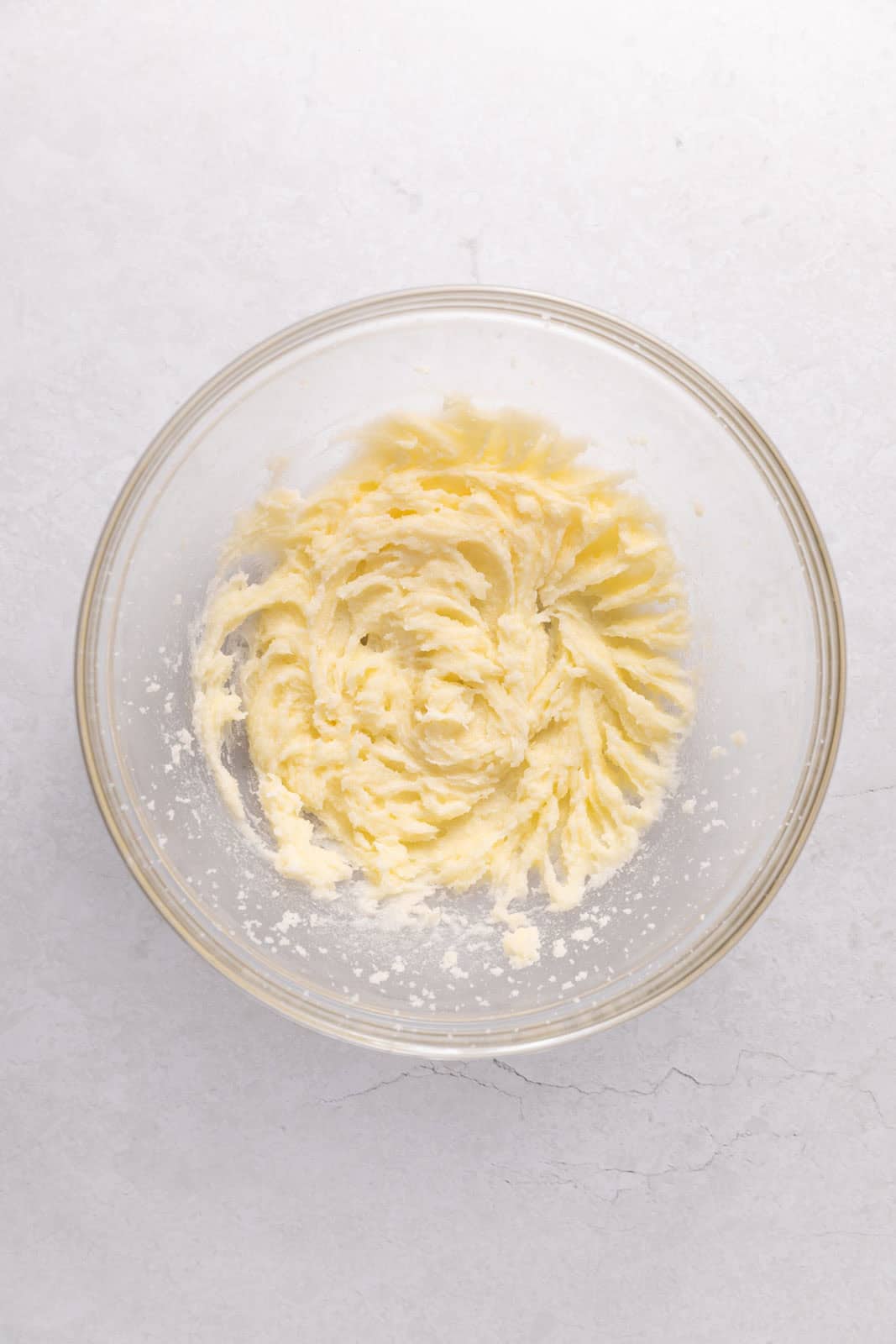 Oil mixed into creamed butter and sugar in a glass mixing bowl set on a flat surface.