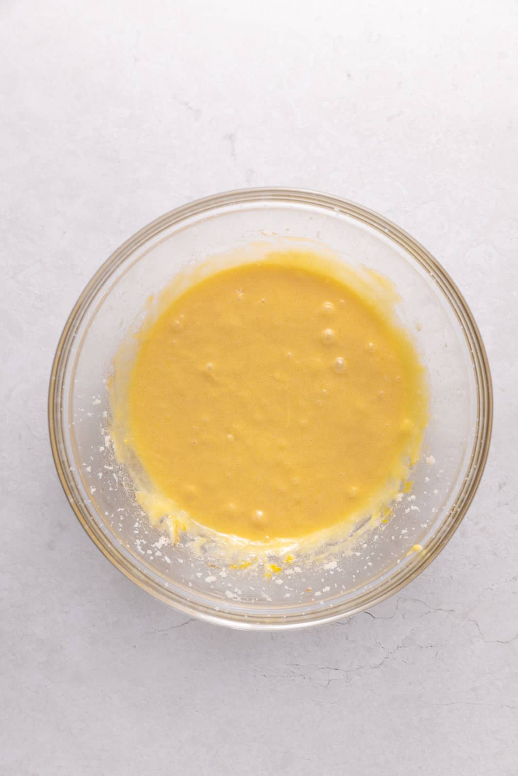 Eggs and vanilla mixed in with butter and sugar in a glass mixing bowl set on a flat surface.