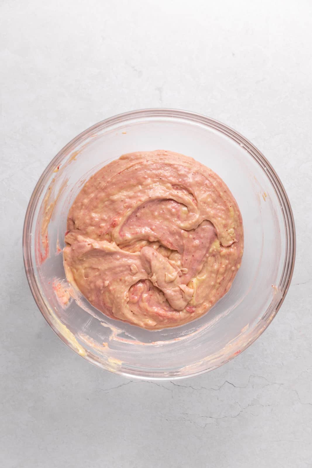Strawberry cupcake batter in a glass mixing bowl set on a flat surface.