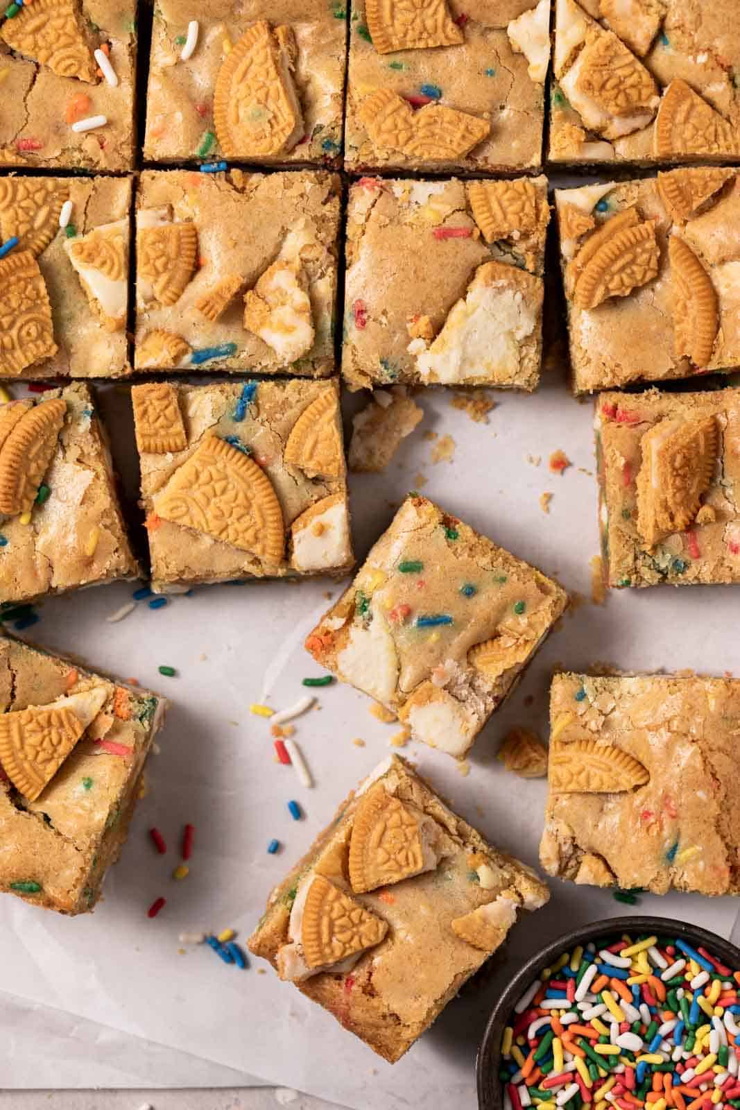 Overhead shot of birthday cake blondes cut into squares with sprinkles around.