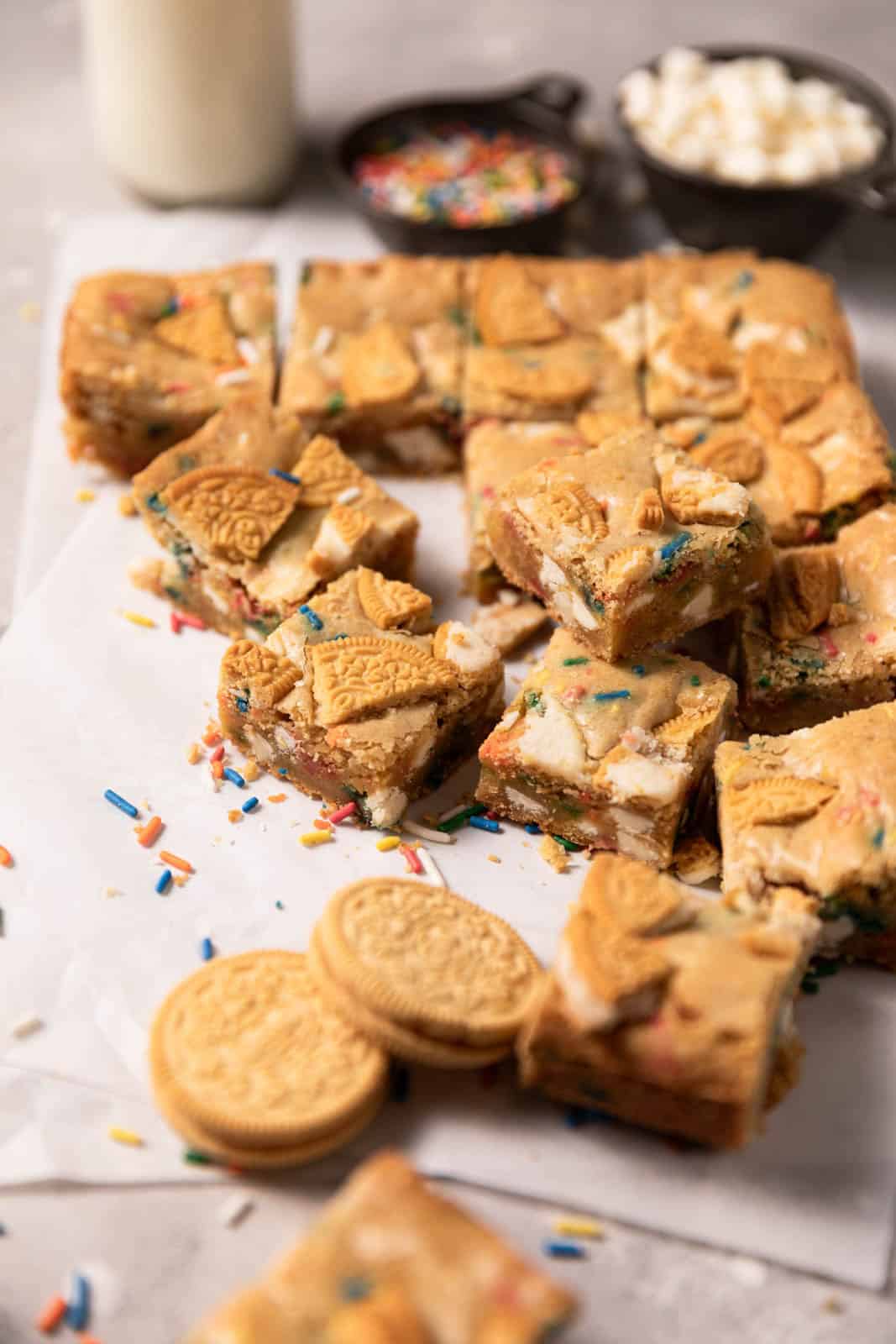 Birthday cake blondie squares set on a flat surface scattered with sprinkles and Golden Oreos.
