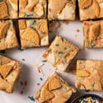 Overhead shot of birthday cake blondes cut into squares with sprinkles around.