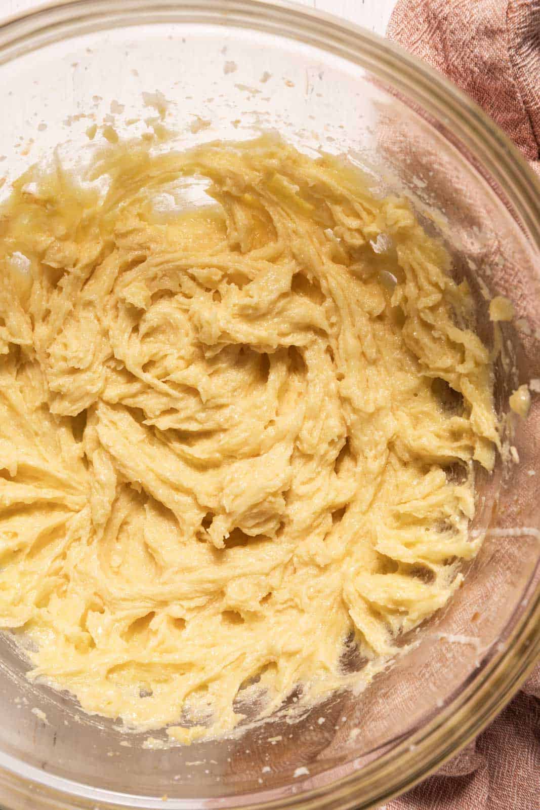 Creamed butter and sugar mixed with eggs and vanilla in a glass mixing bowl.
