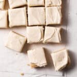 Frosted lemon sugar cookie bars cut into squares and arranged on parchment paper atop a white wooden surface.