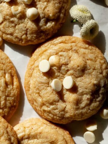 Overhead shot of lemon white chocolate chip cookies set on white parchment paper with small white flowers scattered around.