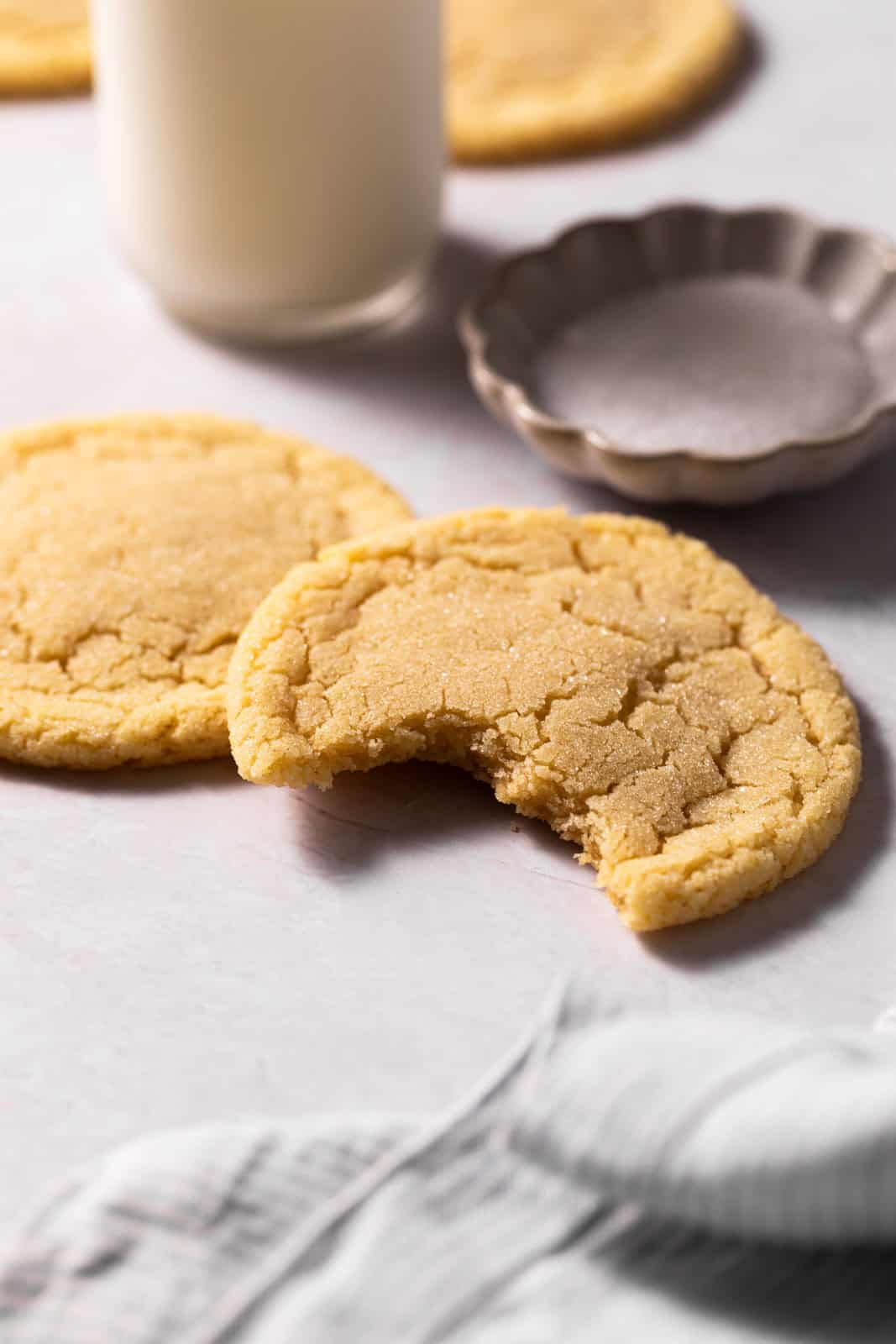 Close up of two small batch sugar cookies on a flat white surface with one missing a bite out of it.