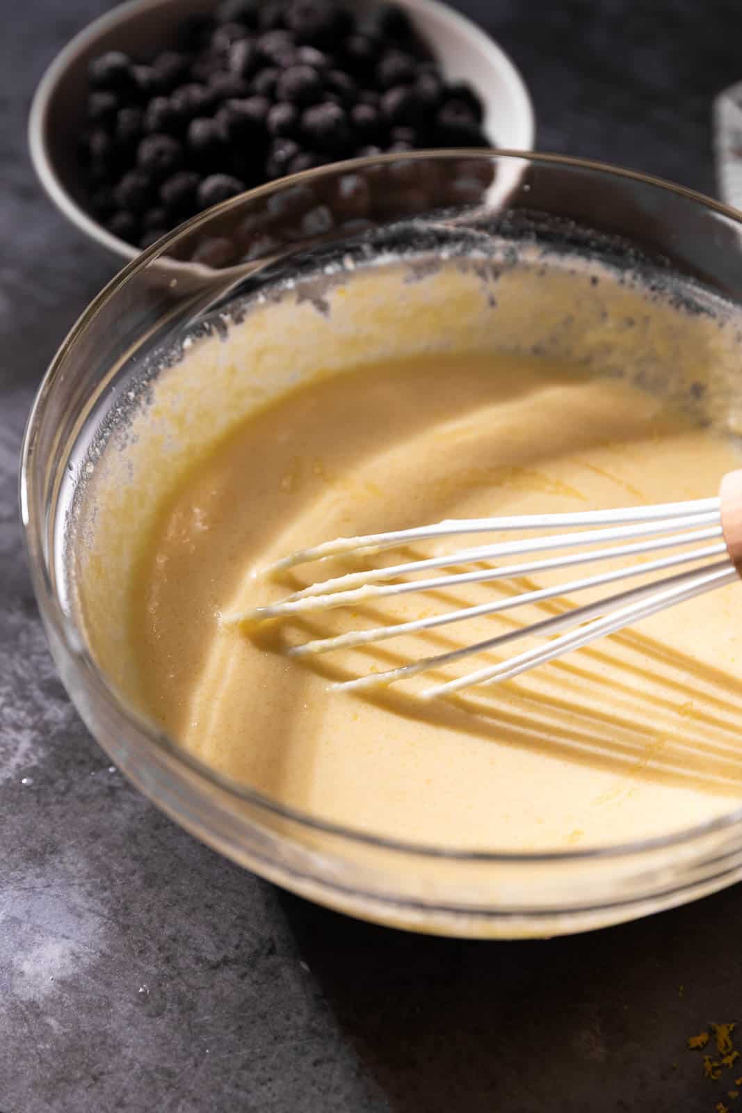 Whisked wet ingredients in a glass mixing bowl with a white whisk.