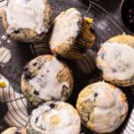 Overhead shot of a wild blueberry lemon poppy seeds muffins with a lemon glaze stacked on a round wire cooling rack with a striped linen on the side.
