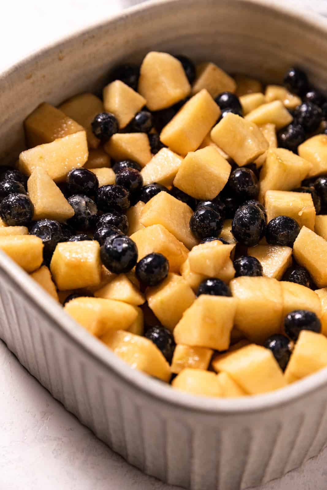 Square deep baking dish filled with apples and blueberries mixed with brown sugar.