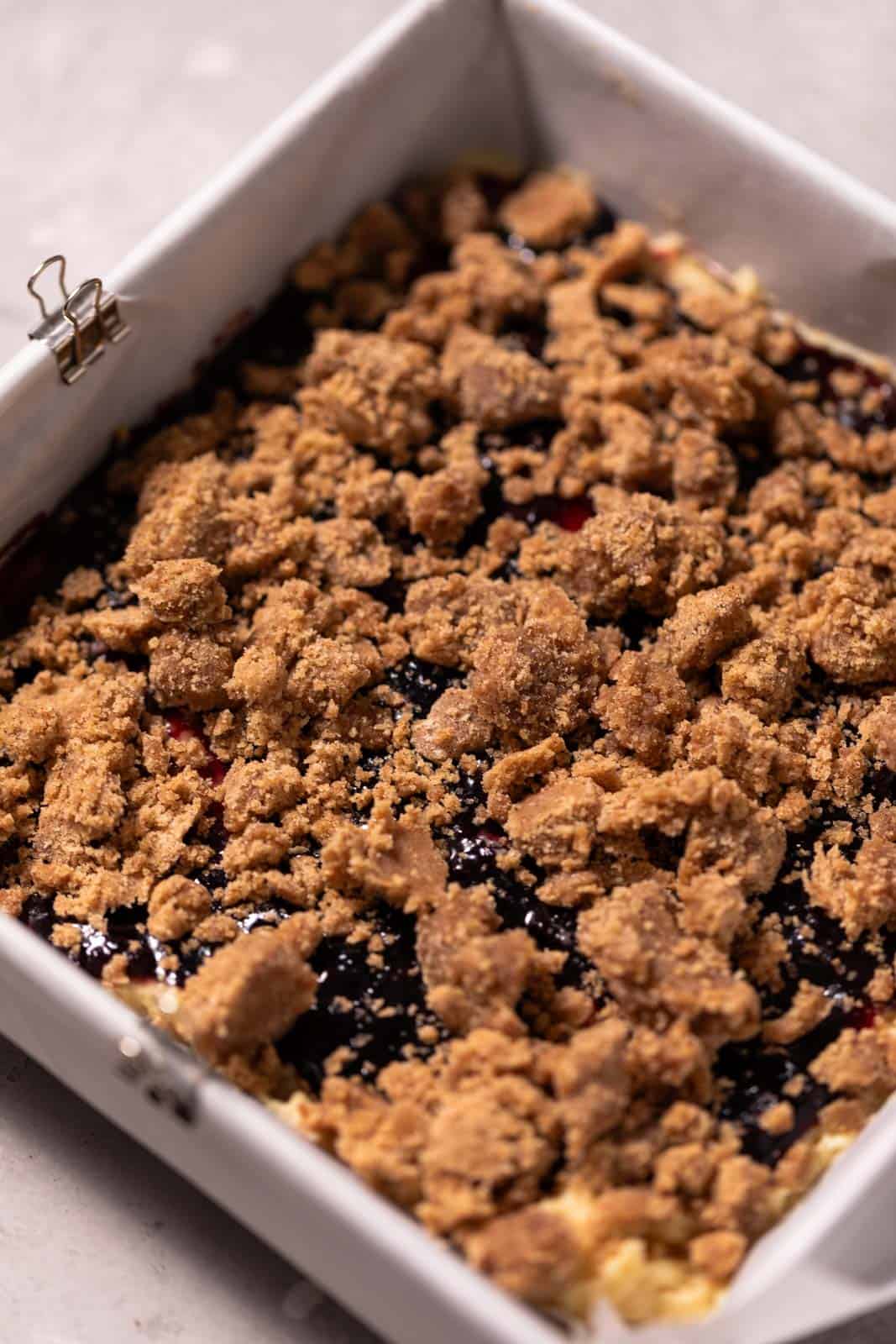 Coffee cake layered with blackberry jam and brown sugar crumble in a square parchment lined baking pan.