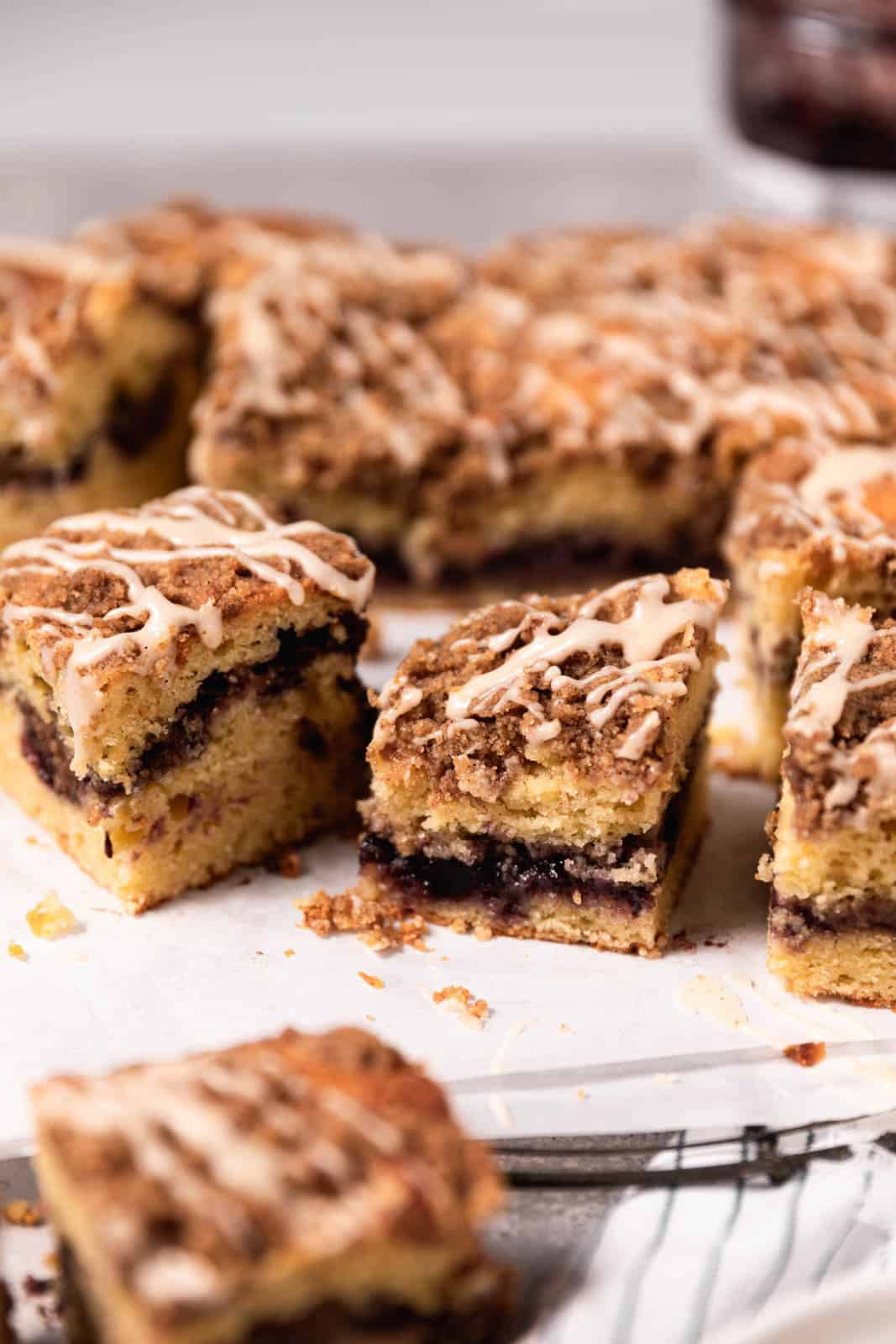 Blackberry coffee cake with vanilla glaze cut into square arranged on white parchment paper.
