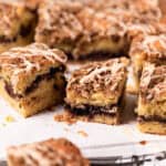 Blackberry coffee cake with vanilla glaze cut into square arranged on white parchment paper.