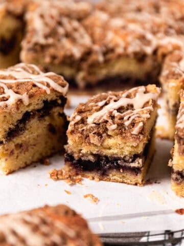 Blackberry coffee cake with vanilla glaze cut into square arranged on white parchment paper.