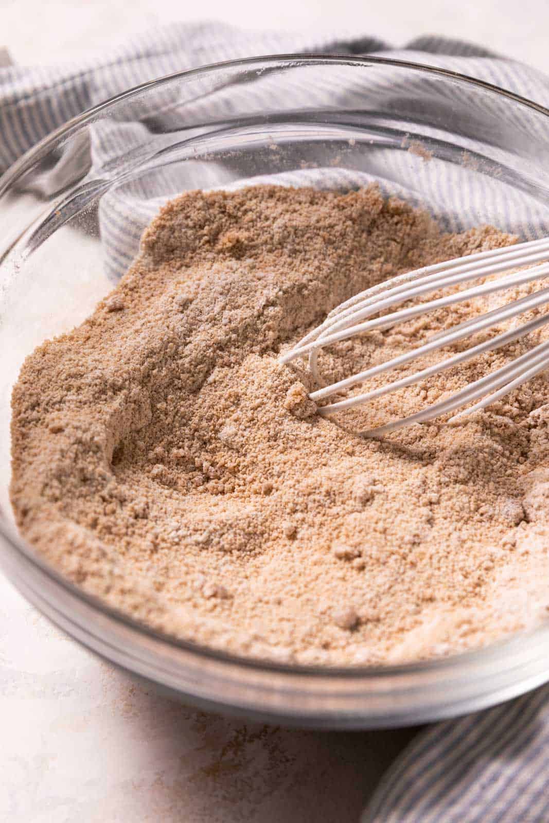 Whisked dry ingredients for crumble topping in a glass mixing bowl with a white wire whisk.